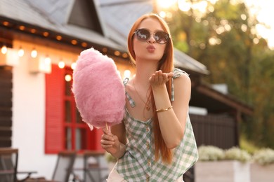 Photo of Woman with cotton candy blowing kiss outdoors on sunny day