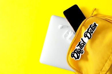 Photo of Different gadgets in bag with words DIGITAL DETOX on yellow background, flat lay. Space for text