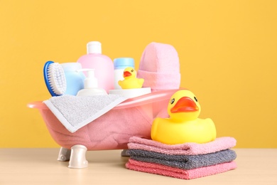 Photo of Baby cosmetic products, toys and towels on table against color background