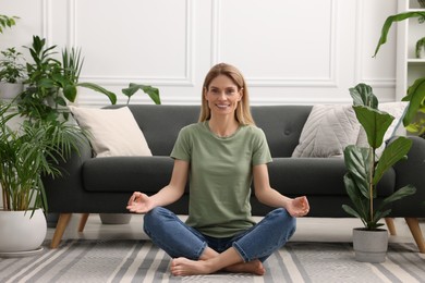 Photo of Woman meditating surrounded by beautiful potted houseplants at home