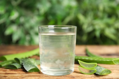 Photo of Fresh aloe drink in glass and leaves on wooden table