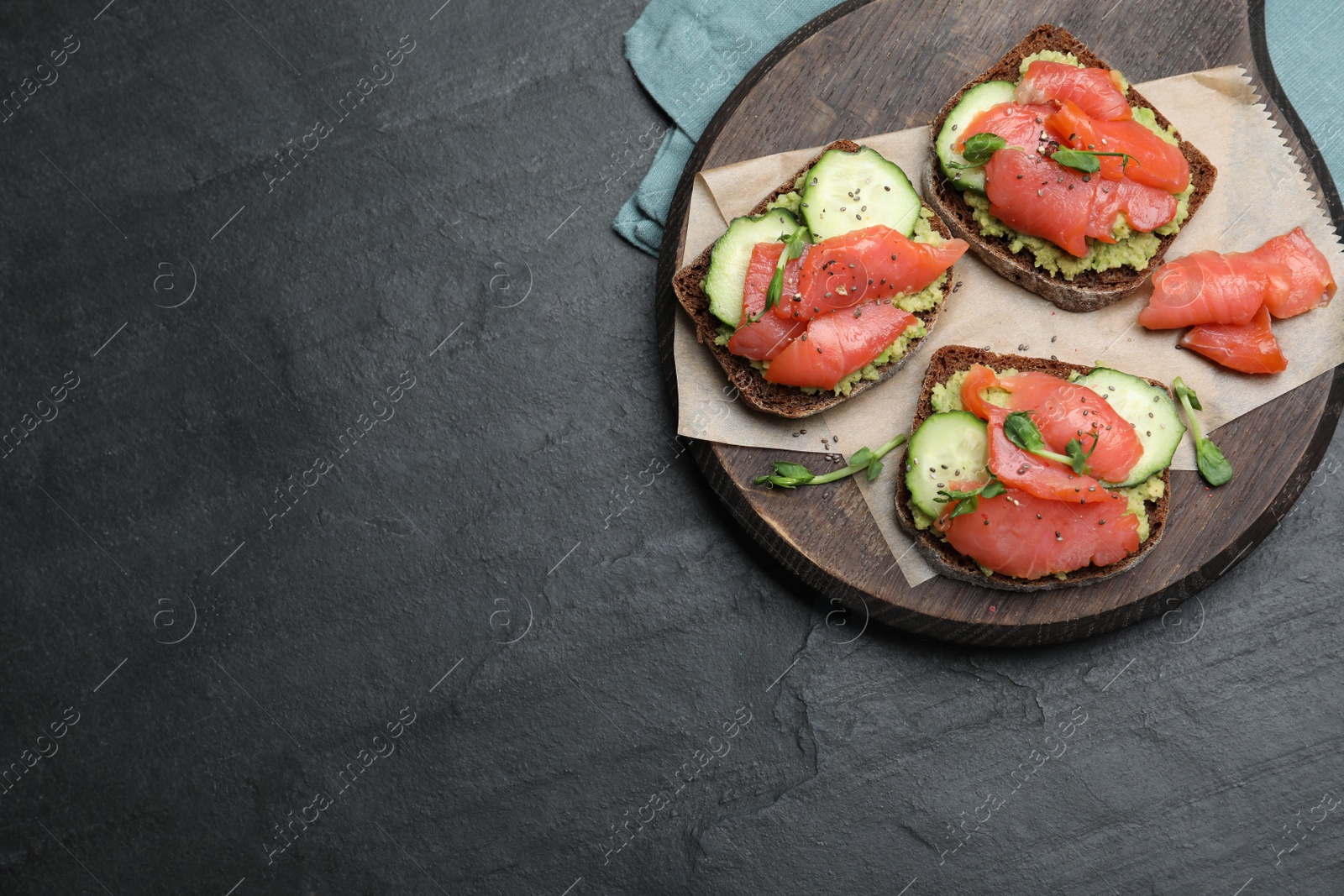 Photo of Tasty bruschettas with salmon, guacamole and microgreens on black table, top view. Space for text