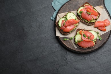 Tasty bruschettas with salmon, guacamole and microgreens on black table, top view. Space for text