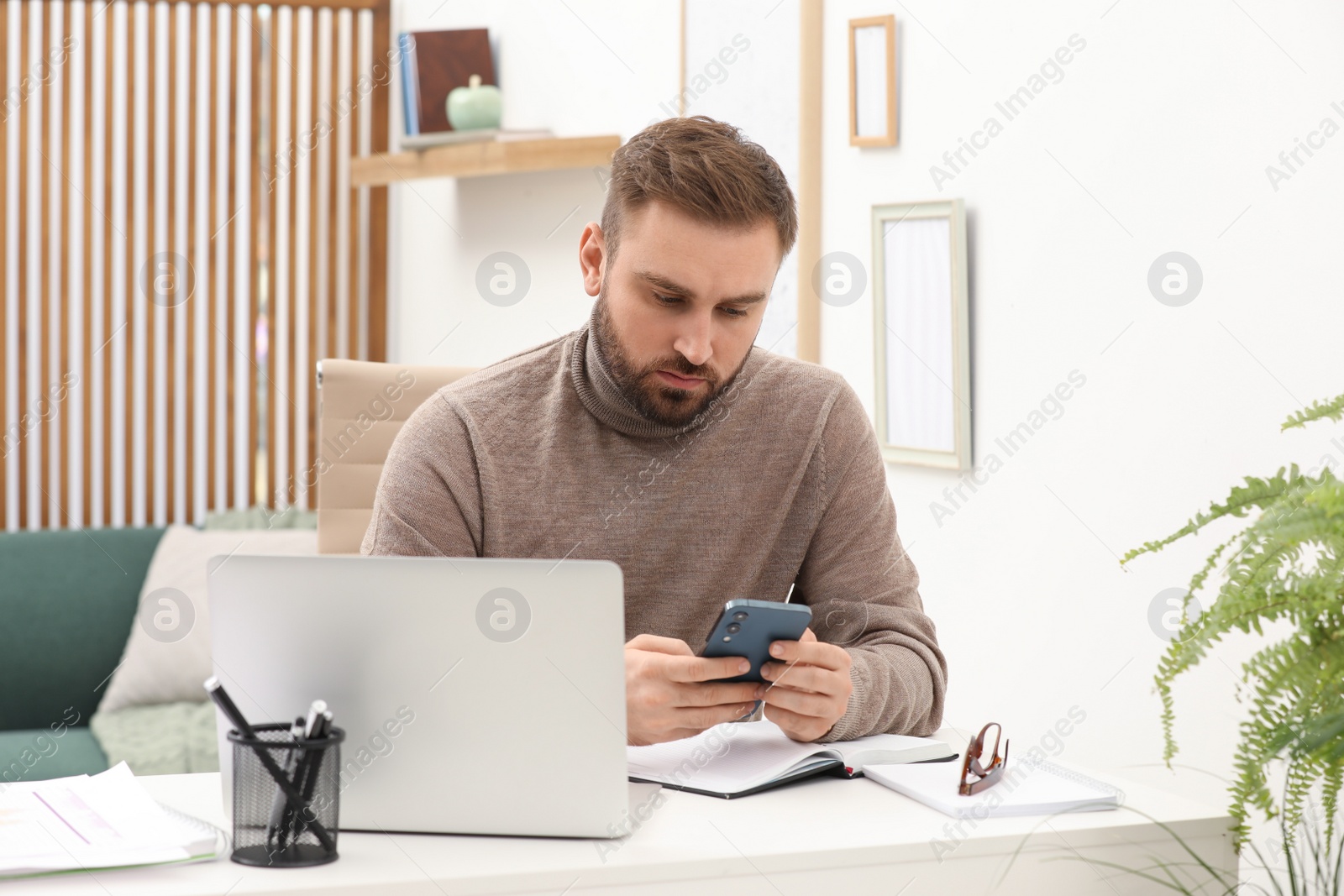 Photo of Young man using smartphone while working at home