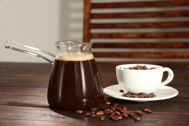 Glass turkish coffee pot with hot drink and beans on wooden table