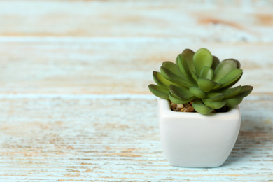 Artificial plant in white flower pot on light blue wooden table. Space for text