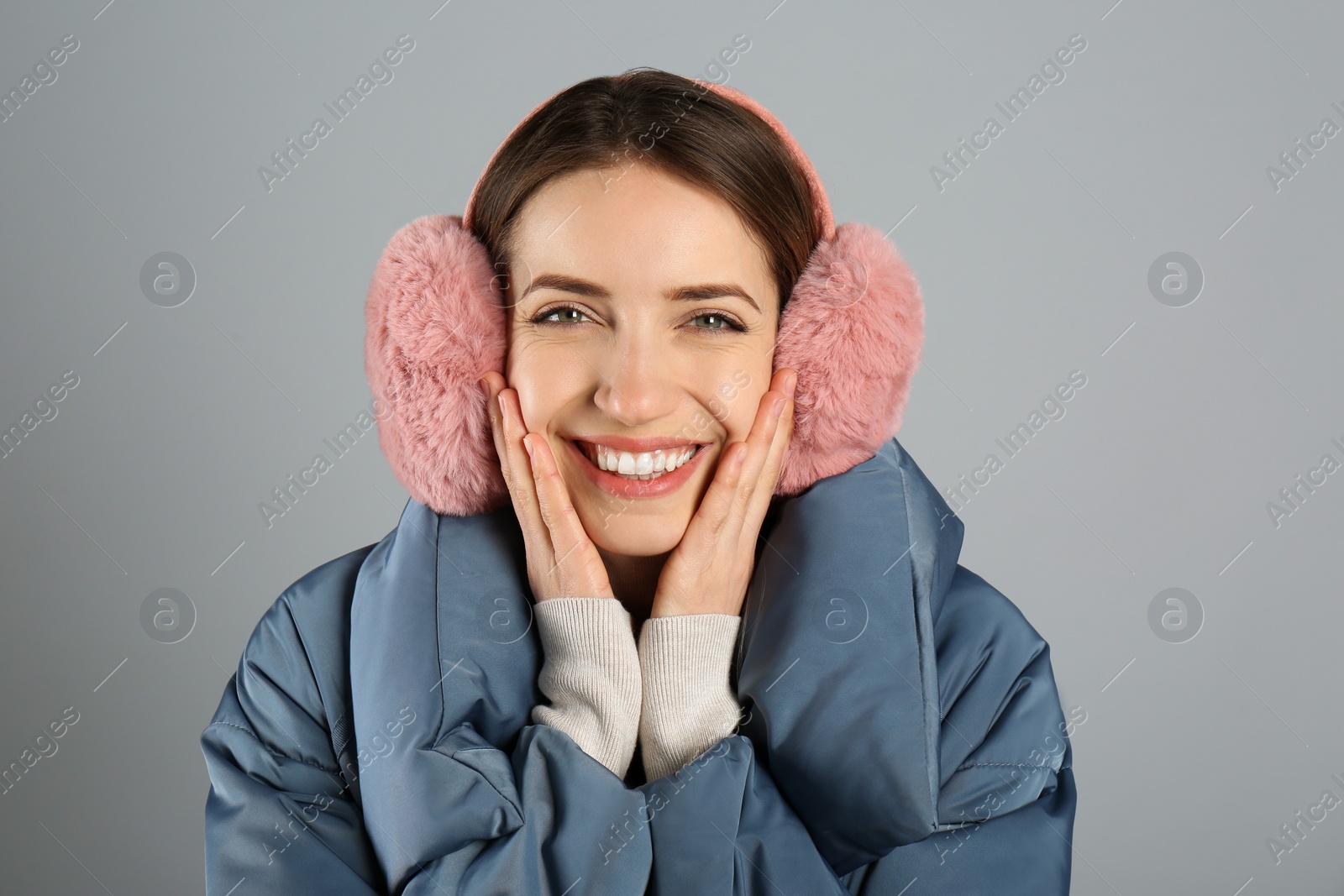 Photo of Happy woman wearing warm earmuffs on grey background