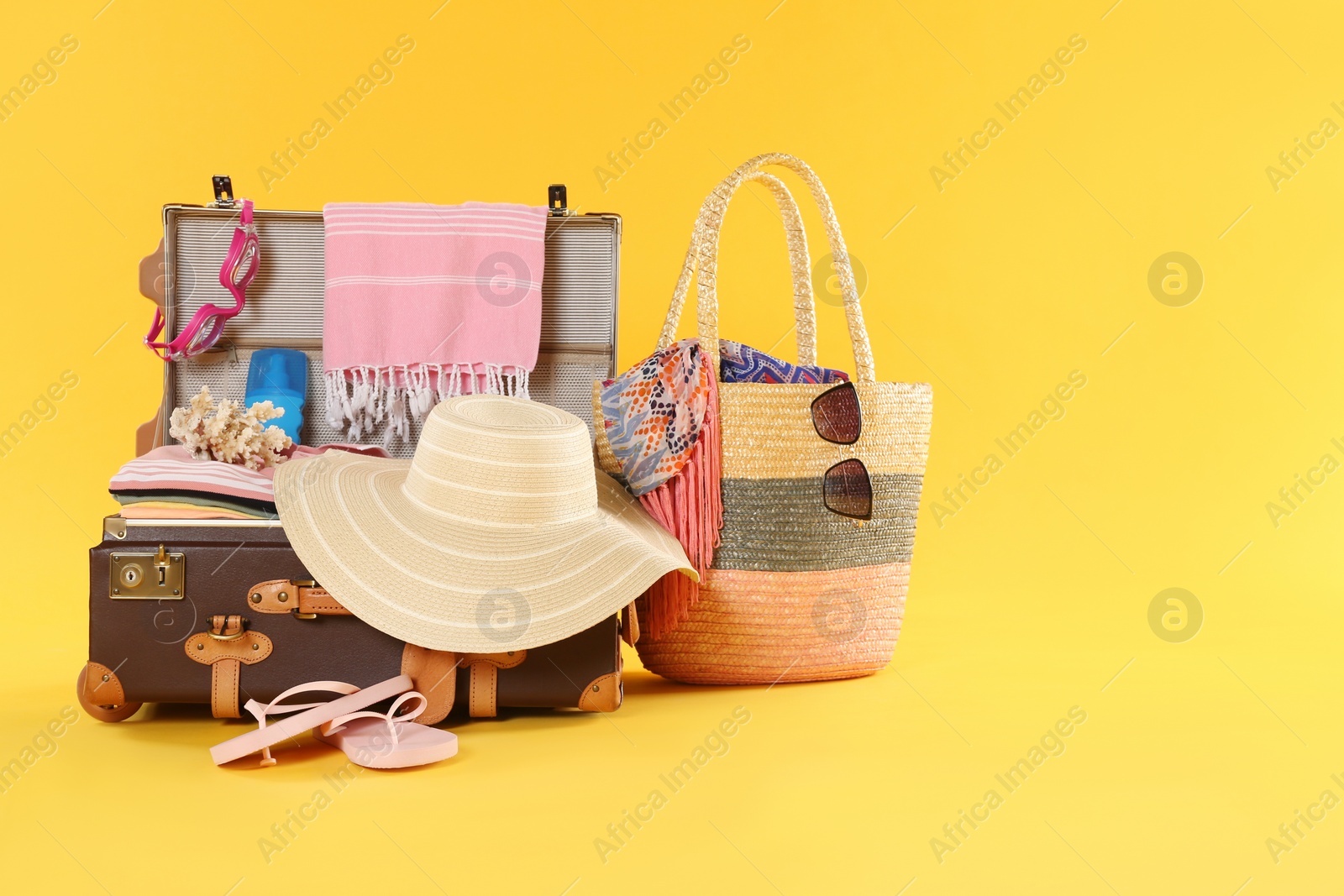 Photo of Bag and open vintage suitcase with different beach objects packed for summer vacation on orange background