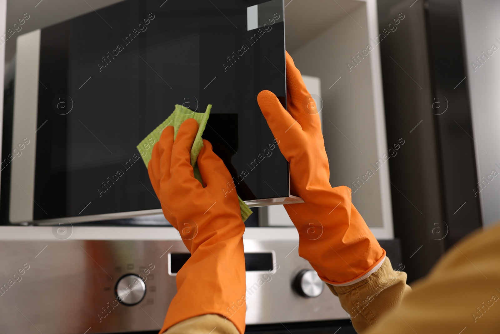 Photo of Woman with microfiber cloth cleaning microwave in kitchen, closeup