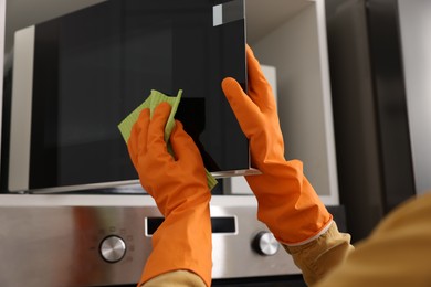 Photo of Woman with microfiber cloth cleaning microwave in kitchen, closeup