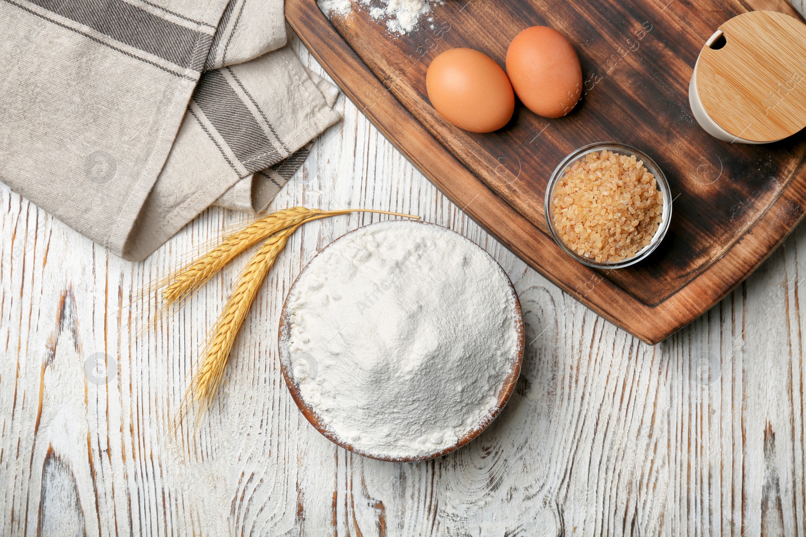 Photo of Bowl with flour, eggs and brown sugar on wooden background, top view