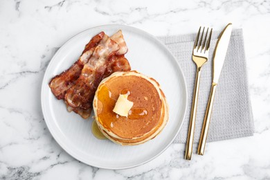 Delicious pancakes with maple syrup, butter and fried bacon on white marble table, flat lay