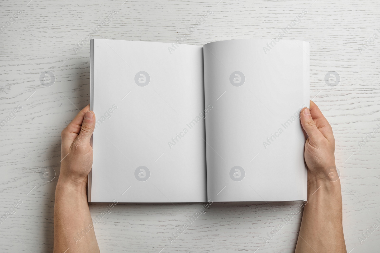 Photo of Woman holding brochure with blank pages on wooden background, top view. Mock up for design