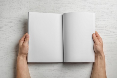 Woman holding brochure with blank pages on wooden background, top view. Mock up for design