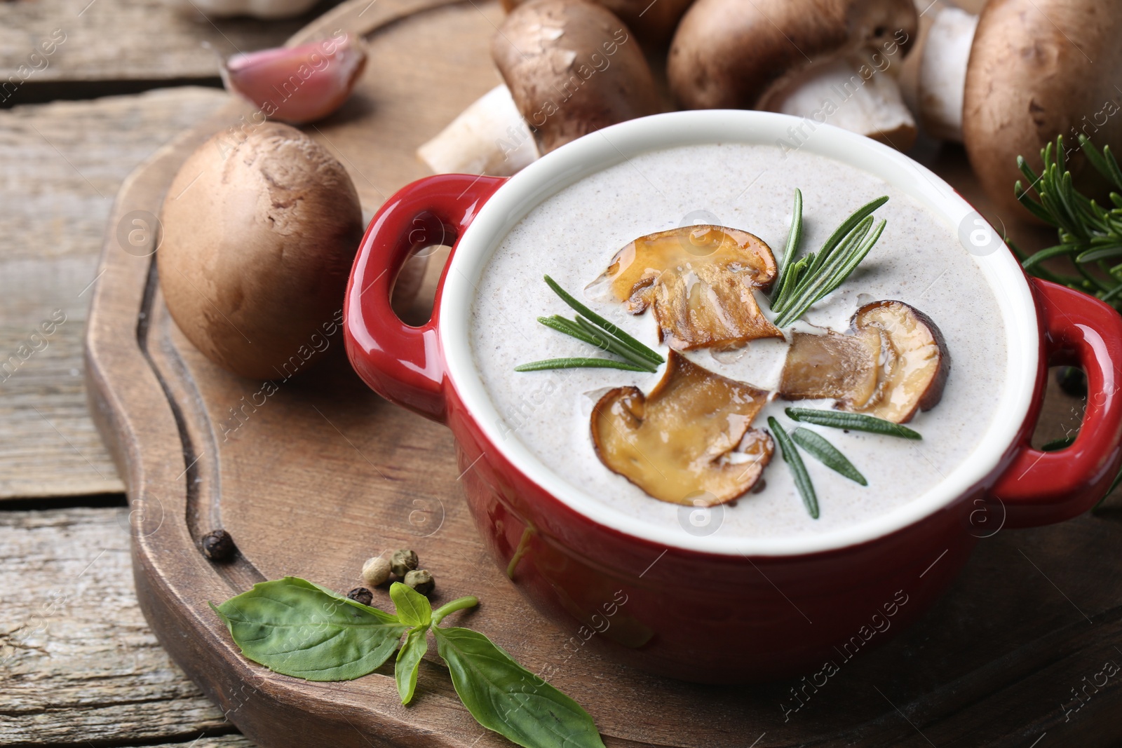 Photo of Delicious homemade mushroom soup in ceramic pot and fresh ingredients on wooden table