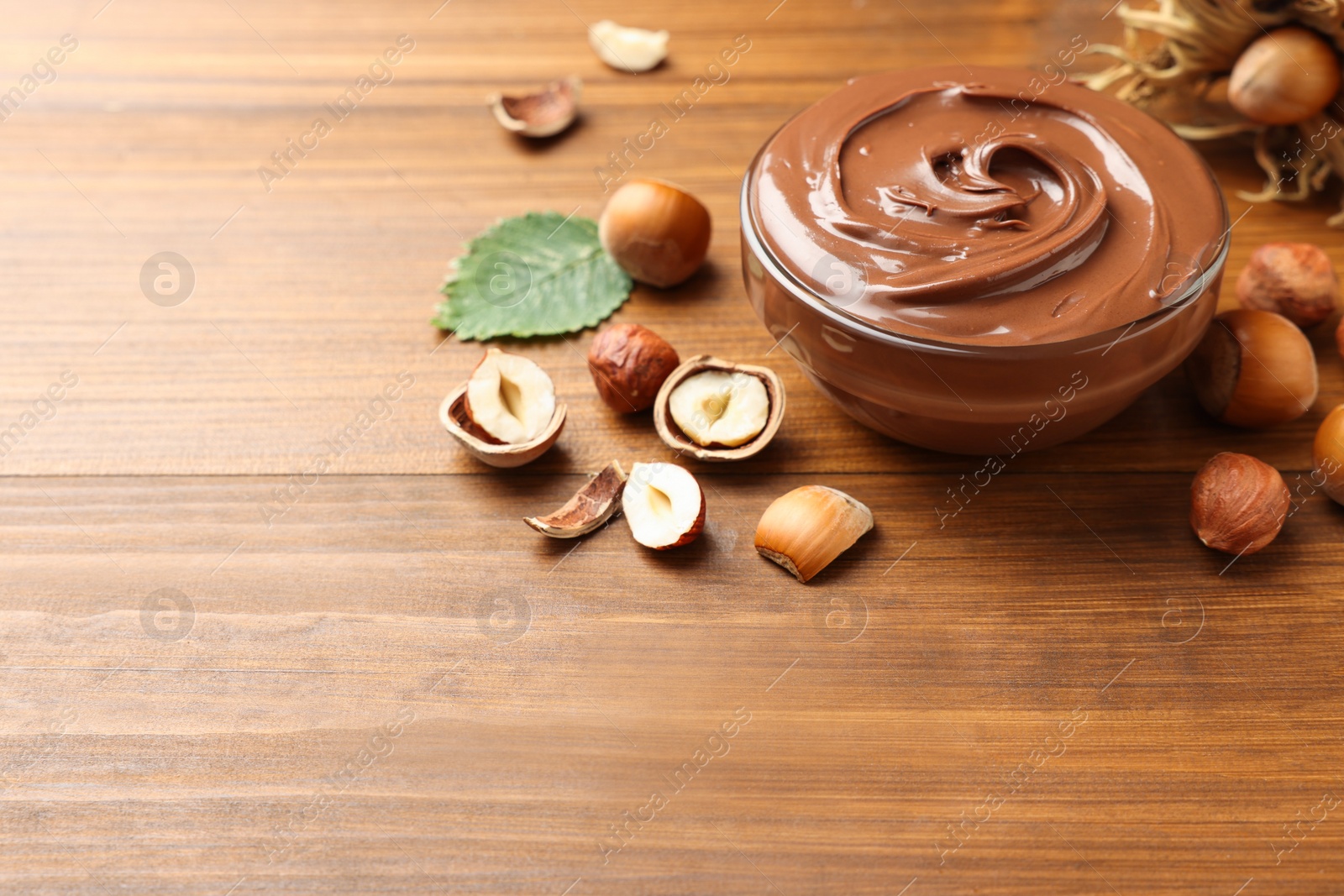 Photo of Glass bowl with tasty chocolate hazelnut spread and nuts on wooden table. Space for text