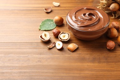 Glass bowl with tasty chocolate hazelnut spread and nuts on wooden table. Space for text