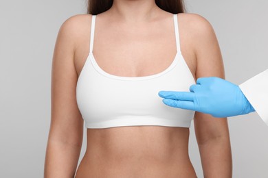 Mammologist checking woman's breast on light grey background, closeup