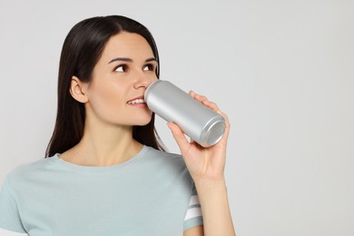 Beautiful young woman drinking from tin can on light grey background. Space for text