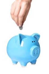 Photo of Woman putting coin into light blue piggy bank on white background, closeup