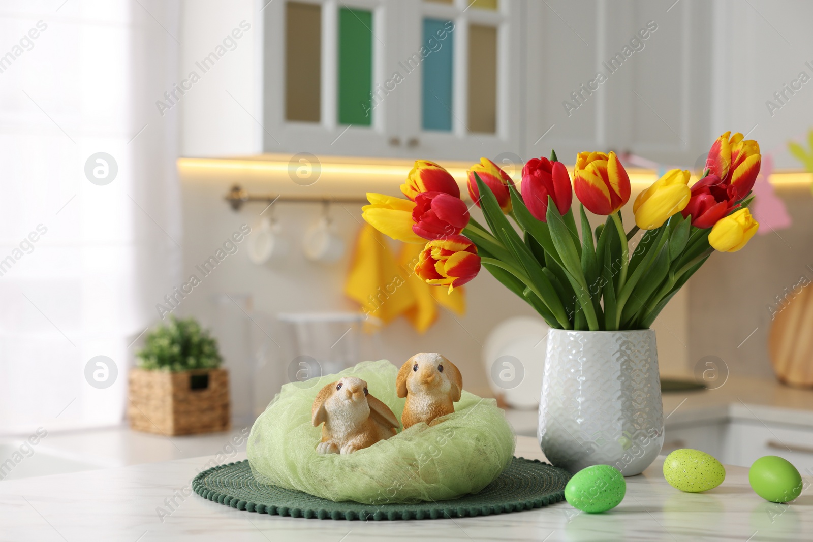 Photo of Easter decorations. Bouquet of tulips, painted eggs and bunny figures on table indoors. Space for text