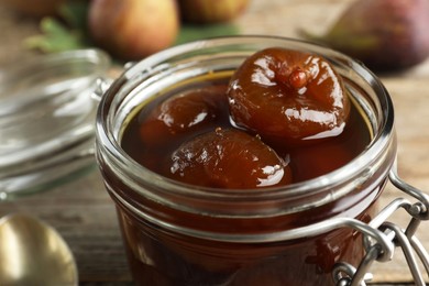 Photo of Jar of tasty sweet fig jam on wooden table, closeup