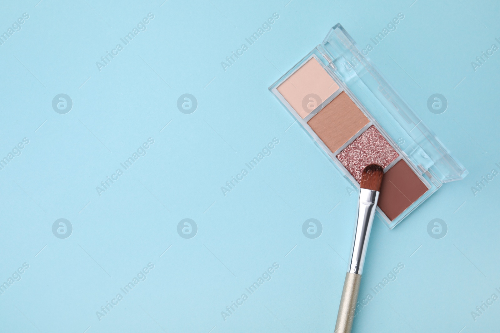 Photo of Beautiful eye shadow palette and brush on light blue background, top view. Space for text