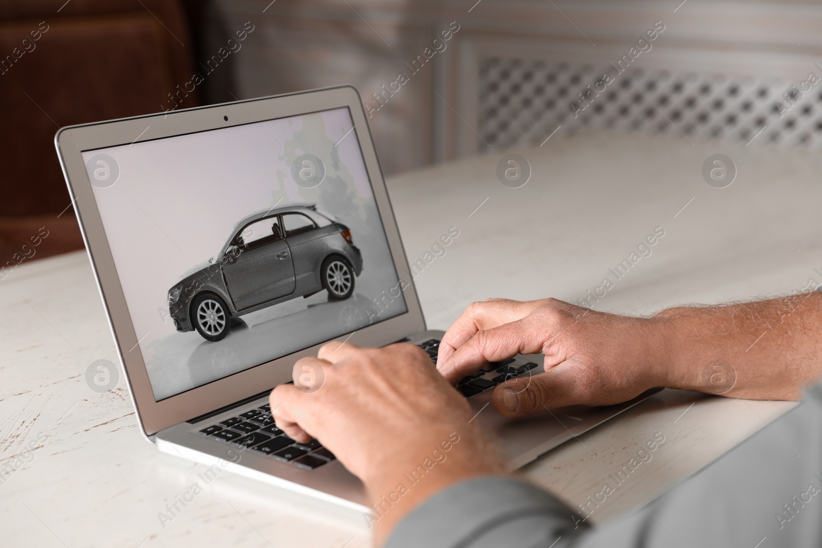 Photo of Man using laptop to buy car at wooden table indoors, closeup