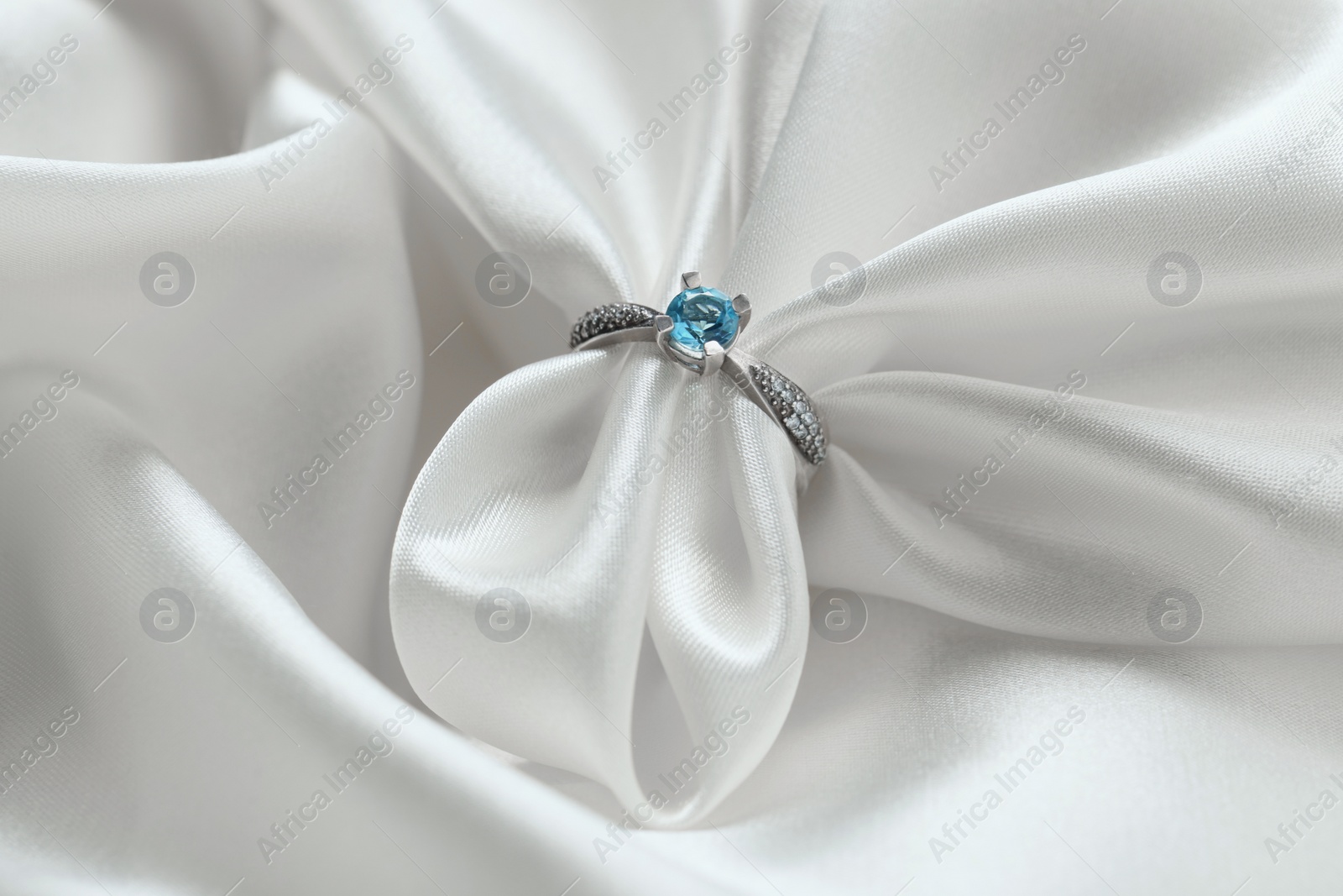 Photo of Beautiful ring with light blue gemstone on white fabric. Luxury jewelry