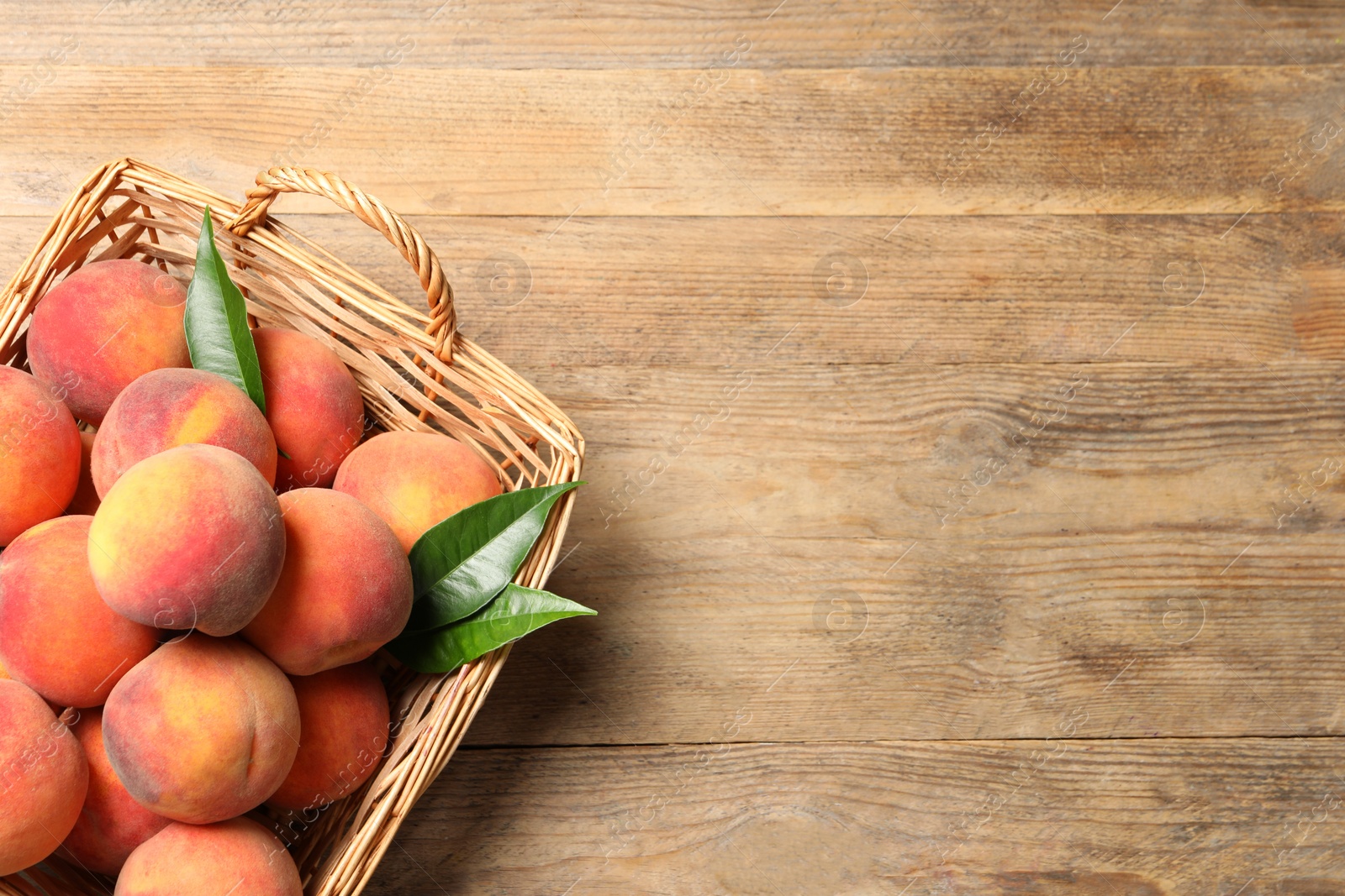 Photo of Fresh peaches and leaves in basket on wooden table, top view. Space for text