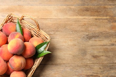 Photo of Fresh peaches and leaves in basket on wooden table, top view. Space for text