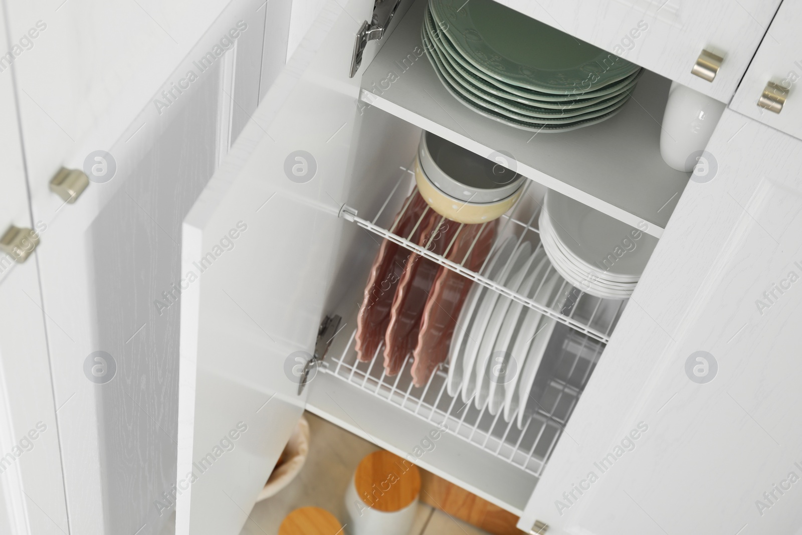 Photo of Clean plates and bowls on shelves in cabinet indoors