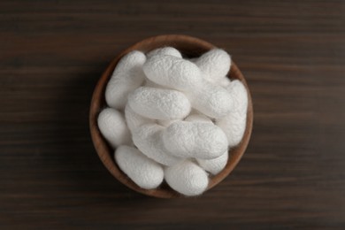 Photo of White silk cocoons in bowl on wooden table, top view