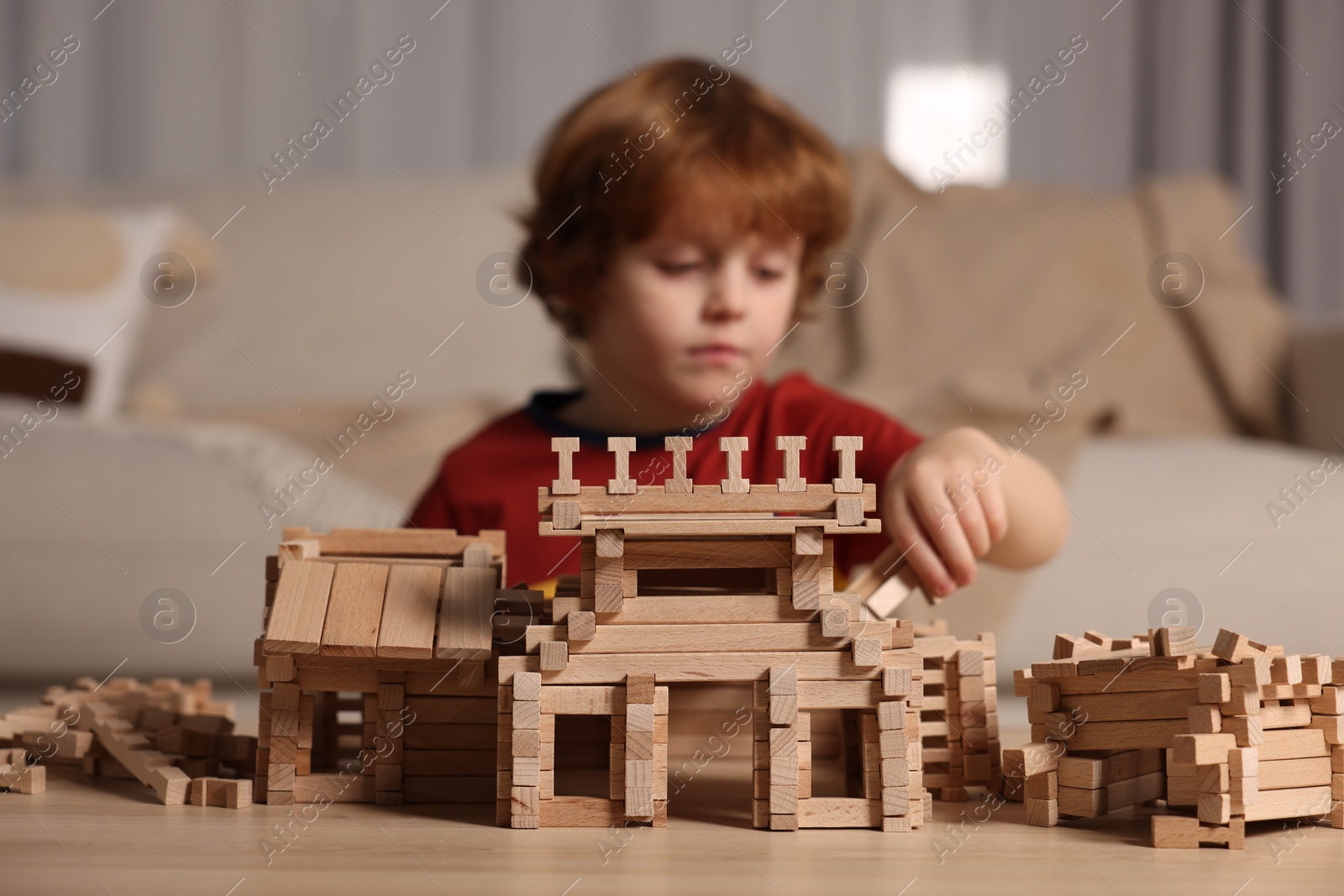 Photo of Cute little boy playing with wooden construction set at table in room, selective focus. Child's toy