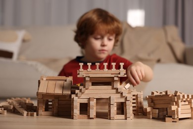 Cute little boy playing with wooden construction set at table in room, selective focus. Child's toy