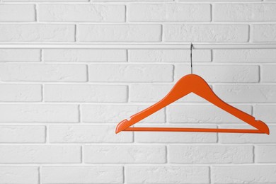 Photo of Orange clothes hanger on rail near white brick wall. Space for text