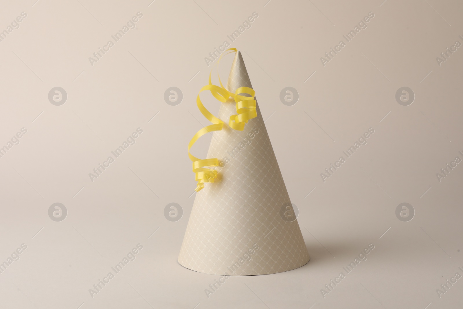 Photo of One beautiful party hat with serpentine streamer on beige background