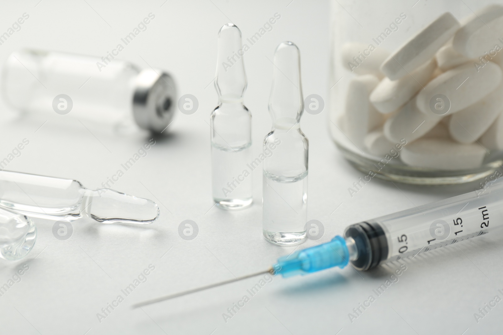 Photo of Glass ampoules with liquid, pills and syringe on white background, closeup