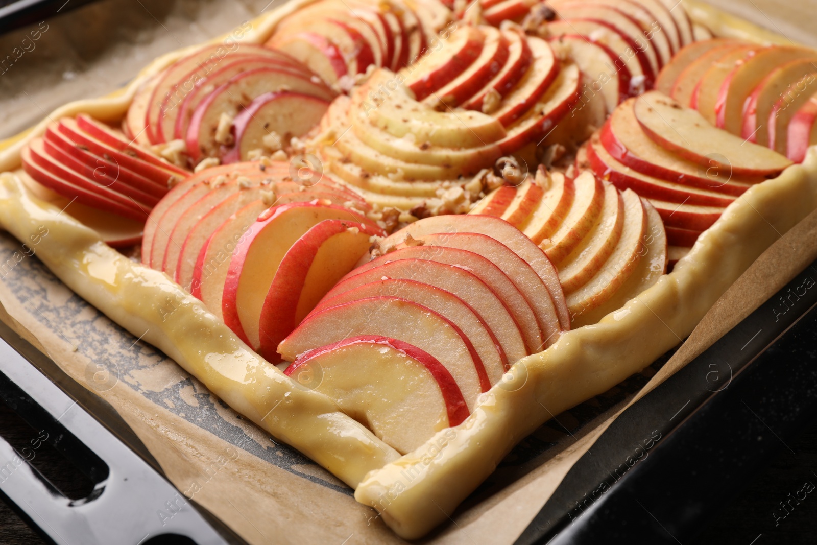 Photo of Uncooked apple galette with nuts on baking tray, closeup