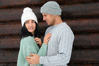 Photo of Lovely couple wearing warm sweaters and hats near wooden wall. Winter season