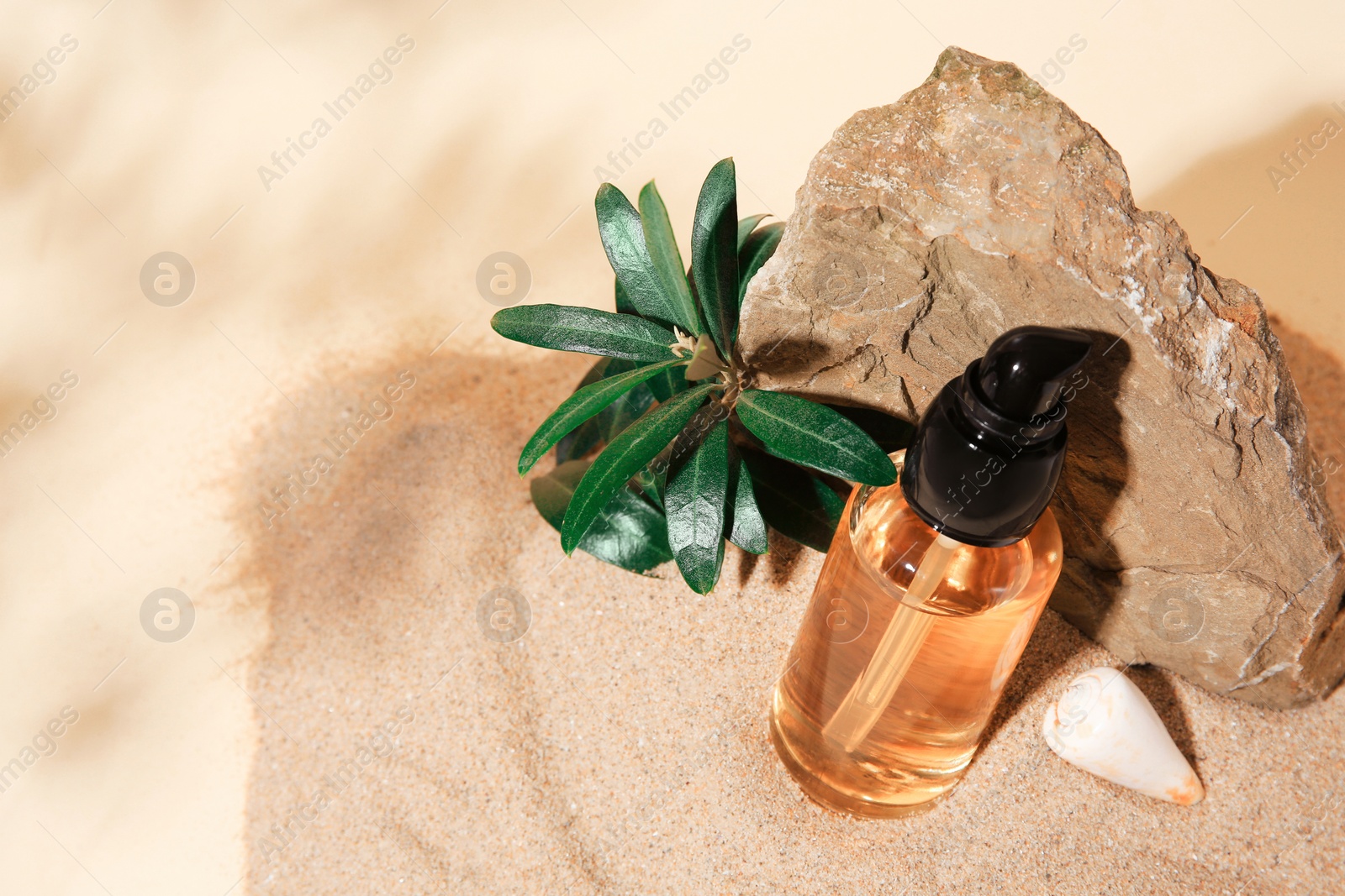 Photo of Bottle of serum, stone and green leaves on sand against beige background. Space for text