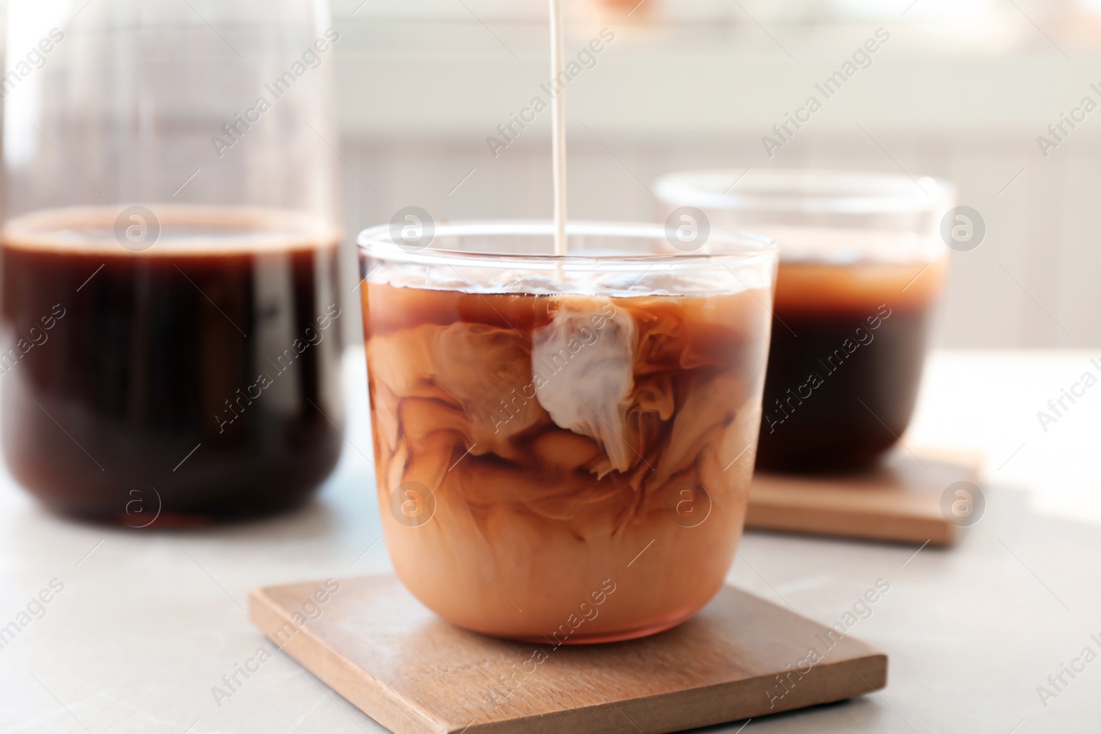 Photo of Pouring milk into glass with cold brew coffee on table