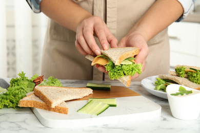 Photo of Woman making tasty sandwich at white marble table, closeup