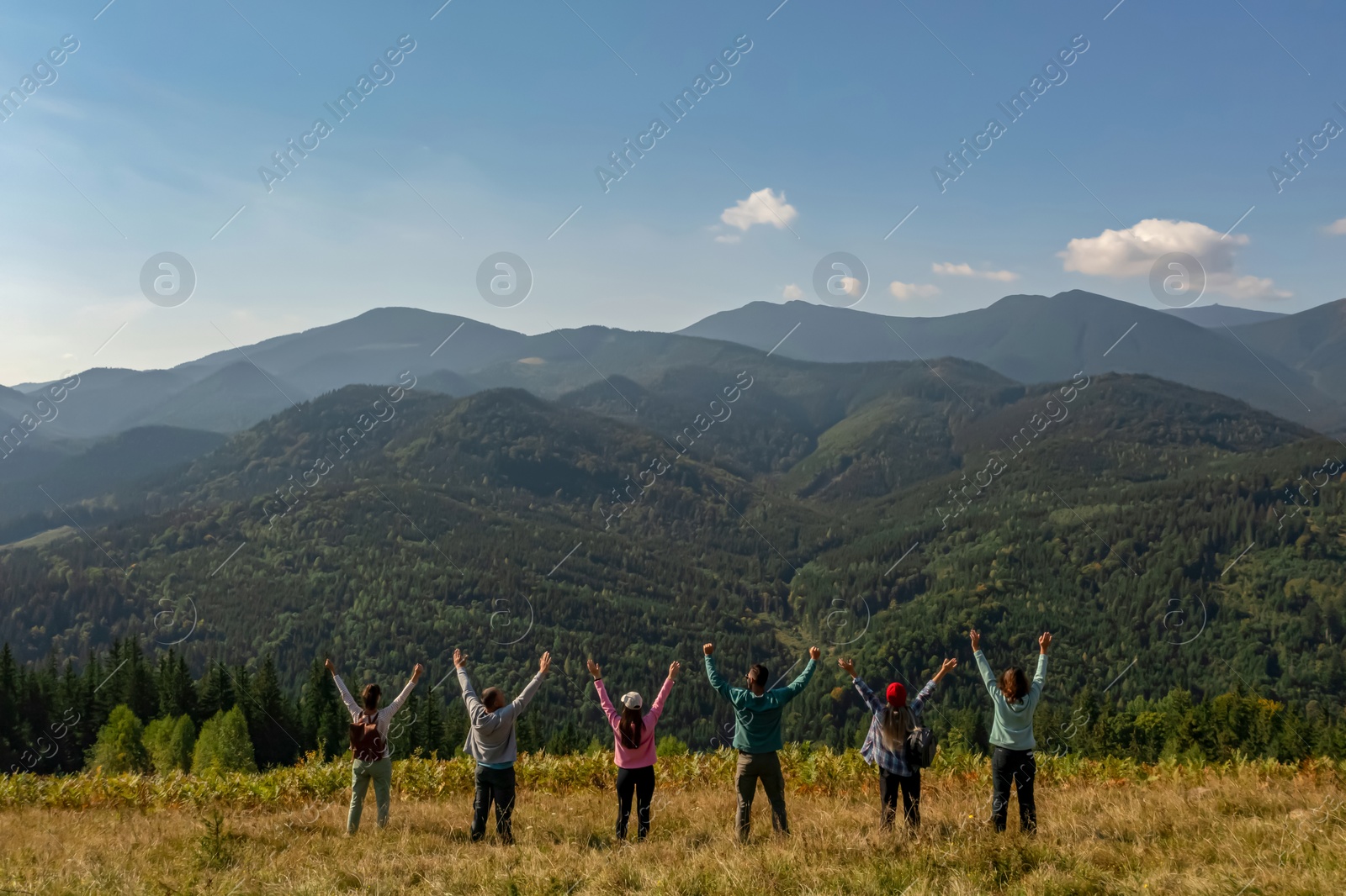 Image of Group of happy tourists on hill in mountains, back view