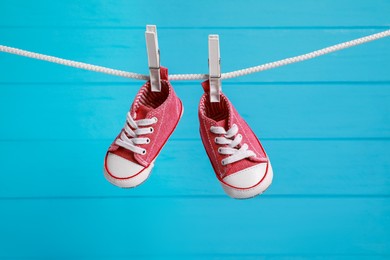 Photo of Cute baby sneakers drying on washing line against light blue wooden wall
