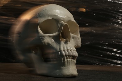 Human skull with stretch film on stone surface against black background