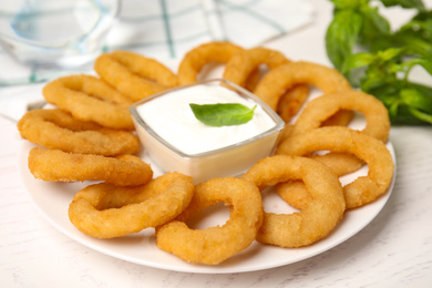 Photo of Delicious onion rings with sauce on white wooden table, closeup