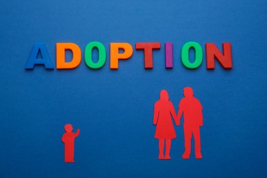 Photo of Figures of parents with child and word Adoption on blue background, flat lay
