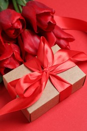 Photo of Beautiful gift box with bow and tulip flowers on red background, closeup