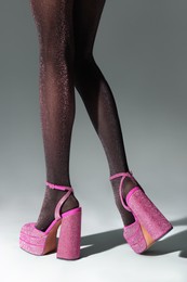 Photo of Woman wearing pink high heeled shoes with platform and square toes on light grey background, closeup
